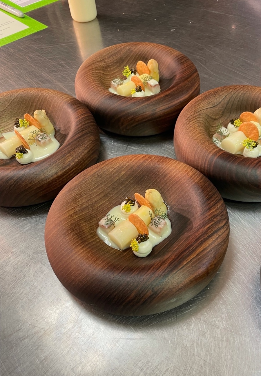 Four plates of white asparagus, caviar and dill in turned wooden bowls on the steel pass